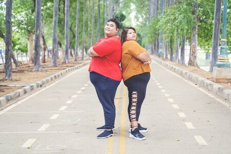 Fat Asian couple wearing sportswear, while posing at camera by crossing their arms proudly on the road at the parkの写真素材