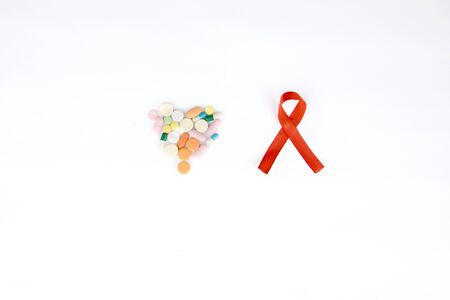 Flat layout of a red ribbon besides heart shaped pills, isolated in white background