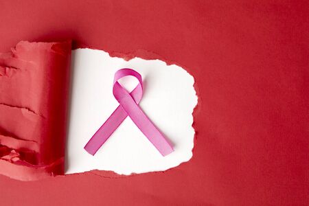 Flat layout of a pink ribbon in a hole of torn red cardboard, isolated in white backgroundの写真素材