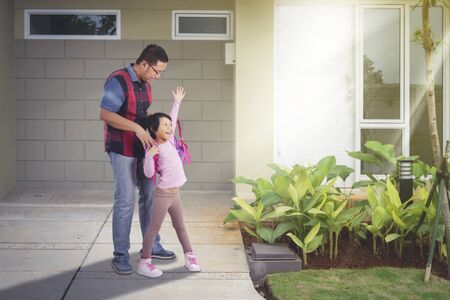 Handsome Asian man wearing backpack for her daughter, while accompanying her back to school at their house yardの写真素材