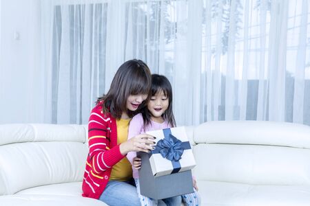 Portrait of happy mother and her daughter open a birthday gift box while sitting on the sofa in the living room at homeの写真素材