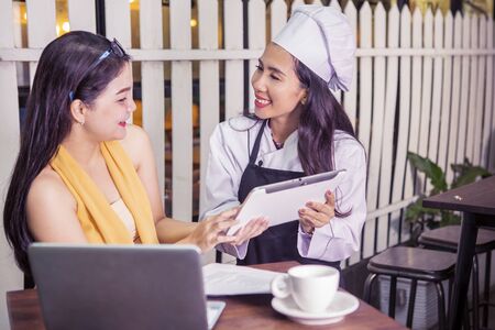 Portrait of beautiful waitress serves menu on digital tablet to her young customer in restaurantの写真素材