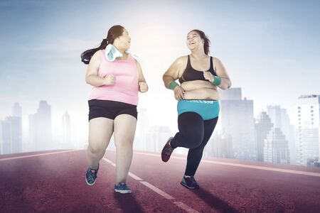 Full length of two happy overweight women running together outdoors at the morningの写真素材