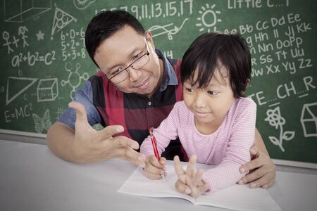 Portrait of handsome Asian man teaching his daughter doing her homework happily in the classroom...