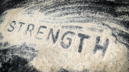 Closeup of STRENGTH text written on white sand with black wooden backgroundの写真素材
