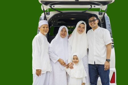 Multi-generation muslim family posing together standing by a car before celebrating Eid Mubarak isolated over green backgroundの写真素材