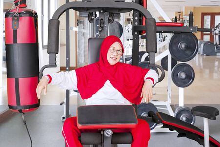 Senior woman sitting on gym machine after workout in the fitness centerの写真素材