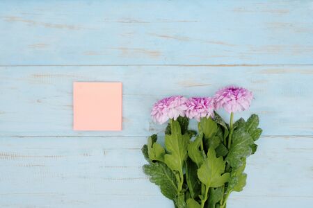Flat lay of pink gerbera flower and empty note on wooden background