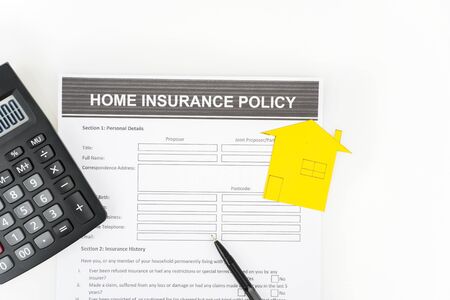 Top down view of home insurance policy concept with calculator, yellow house shaped cardboard, and a pen; isolated in white backgroundの写真素材