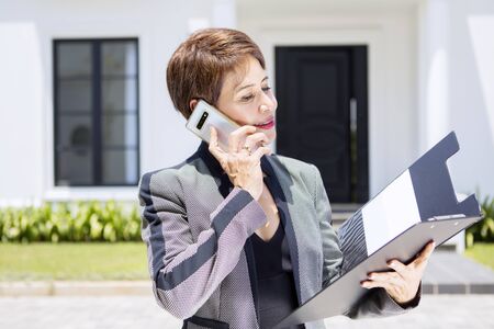Portrait of beautiful senior brunette Asian woman reading her documents, while calling someone out...
