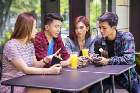 Portrait of group of teenagers sitting in the restaurant while looking at smartphone together