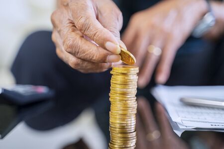 Closeup of elderly man hand stacking golden coins on the tableの写真素材