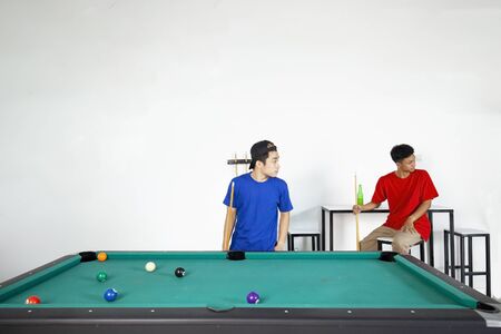Two young Asian men standing and sitting near the pool table