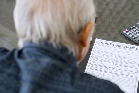 Senior man reading health insurance application form on the table at home
