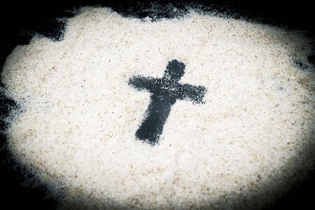 Closeup of cross symbol on the sand with black backgroundの写真素材