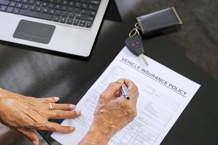 Senior man hand filling a vehicle insurance form on the table at home