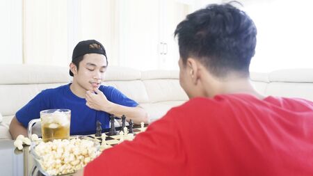 Picture of asian man thinking about chess strategy while playing chess with his friend at homeの写真素材