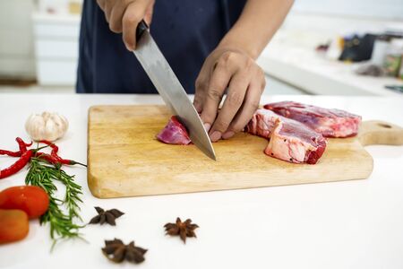 Hand chopping sirloin beef steak with knife on the chopping board in the kitchen