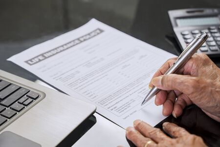 Senior man hand signing a life insurance claim form on the table at home