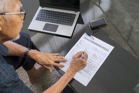 Elderly man filling a vehicle insurance form on the table at home