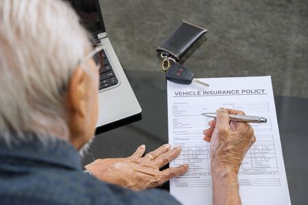 Old man filling a vehicle insurance form on the table at home