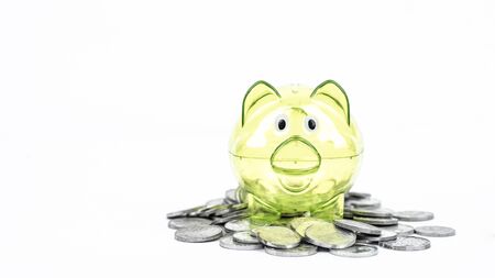 Green transparent piggy bank and pile of coins in the studio, isolated on white backgroundの写真素材
