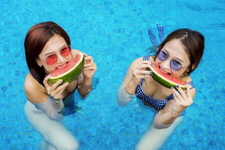 Beautiful young women in swimwear eating watermelon on the swimming pool