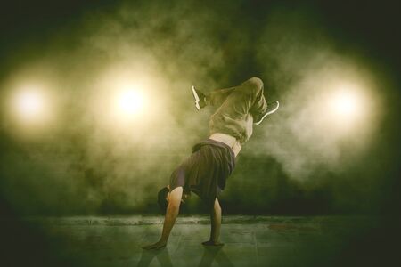 Young man break dancing at night with smoke and lights on the street
