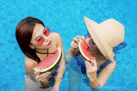 Top view of beautiful young women eating fresh watermelon on the swimming poolの写真素材