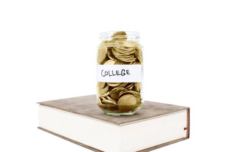 Jar full of golden coins on the book, isolated on white background. Savings for education conceptの写真素材