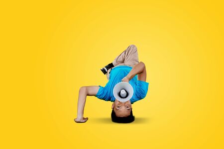 Young man break dancing while speaking with megaphone in the studio with yellow background