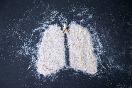 Top view of cigarette butt and lung symbol made of sand on black background