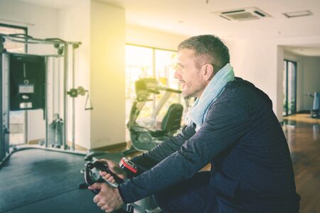 Side view of caucasian man doing workout while sitting on gym cycling in fitness centerの写真素材