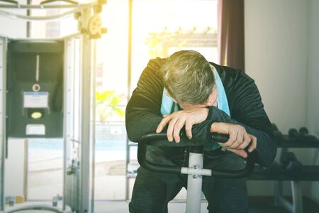 Portrait of mature man sleeping and feeling tired while doing exercise on gym cycling in fitness centerの写真素材