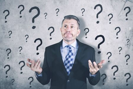 Portrait of confused businessman standing with question mark while wearing formal suitの写真素材