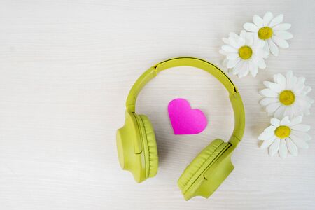 Flat layout of pink heart shaped cardboard in the middle of green headphone & jasmine petals in wooden table backgroundの写真素材