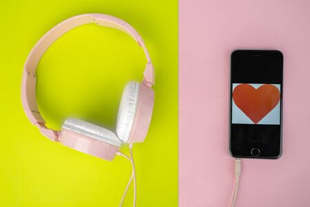 Flat layout of pink headphone connected to the smartphone projecting love image, isolated in dual layer background with yellow and pink colorsの写真素材