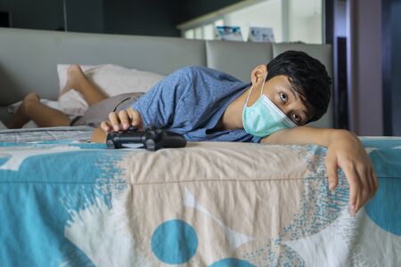 Portrait of little boy feeling bored with video game while doing social distancing at home