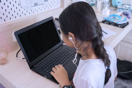 Top view of little student studying at home while using laptop and earphone in her room