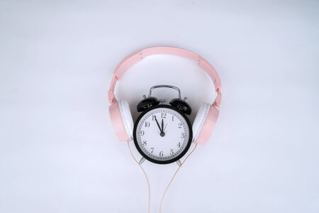 Flat layout of black alarm clock in the middle of pink headphone, isolated in violet backgroundの写真素材