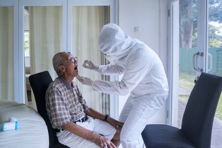 Medical worker doing coronavirus swab test on senior man with a cotton in the hospitalの写真素材