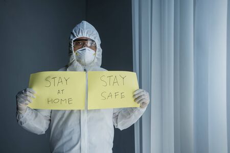 Doctor in hazmat suit showing social message to Stay at Home and Stay Safe during coronavirus outbreakの写真素材