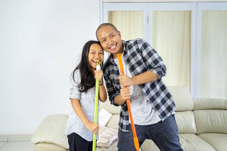 Little girl and her father using a broom and mop as microphone while singing together in the living room. Shot at homeの写真素材