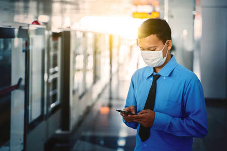 JAKARTA - Indonesia. May 12, 2020: Asian businessman wearing a mask while using a cellphone and waiting the train on the MRT stationのeditorial素材