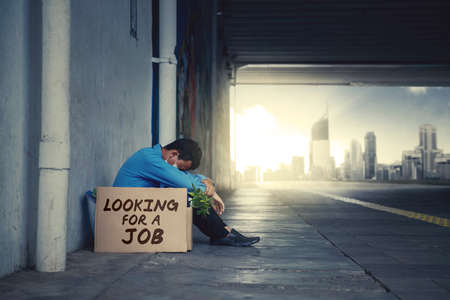 JAKARTA - Indonesia. May 12, 2020: Sad businessman sitting on the road tunnel with cardboard box with text of looking for a job. Covid-19 impact conceptのeditorial素材