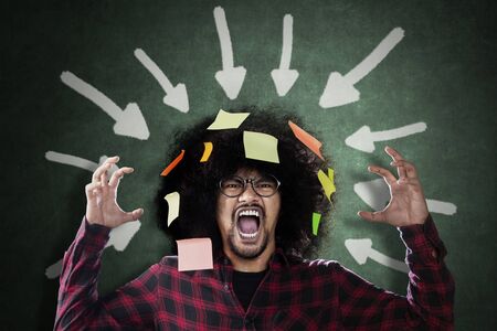 Frustrated Afro man screaming under arrows over his head with blank sticky notes with chalkboard...