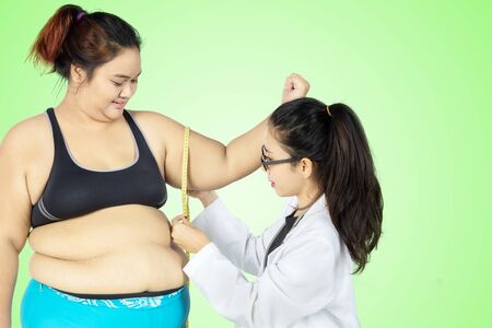 Female physician measuring bicep of her fat patient by using a measure tape while examining in the clinicの写真素材