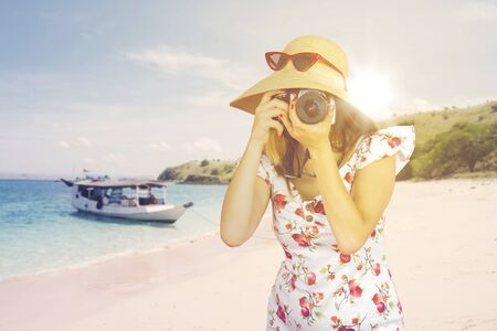 Female tourist taking picture with dslr camera on the beach while wearing summer dress
