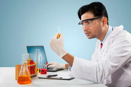 Male researcher holding a test tube while doing an experiment and sitting in the studio