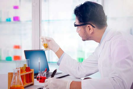 Male scientist doing medical research in the laboratory while holding a test tube and writing on the...